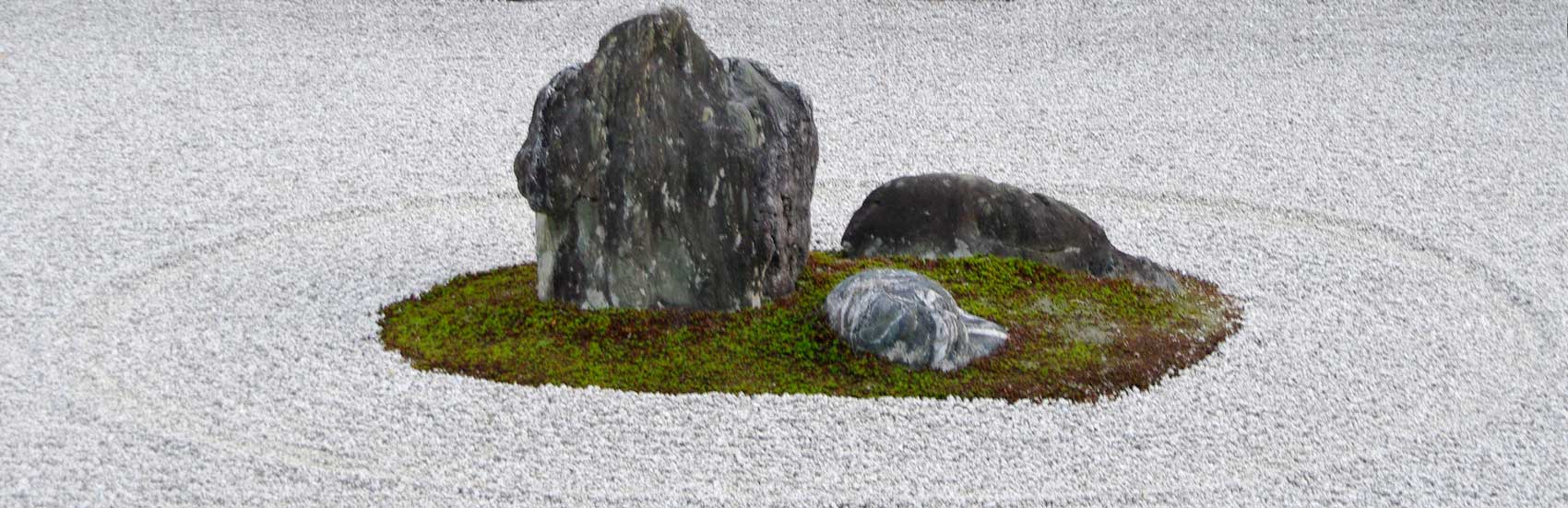 A group of 3 rocks surrounded by raked sand – Ryoan-ji